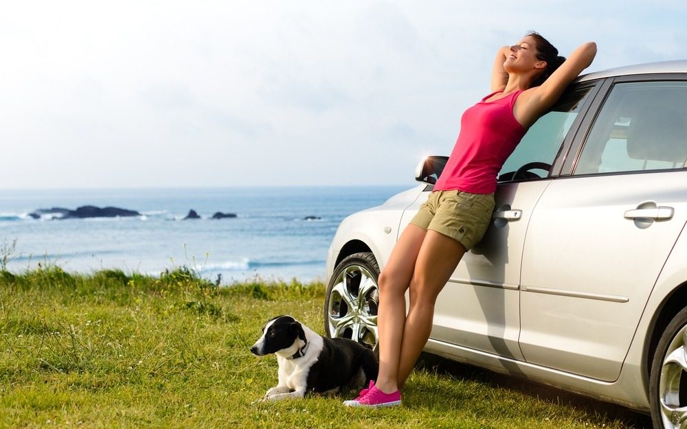 young woman next to her car with her dog at her feet