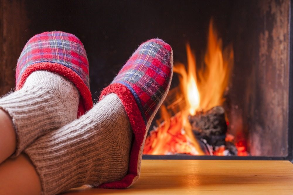 Legs of a person lying down, feet in slippers facing an open fire