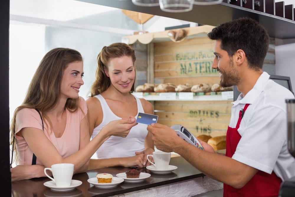 two young women showing their credit card in a bar