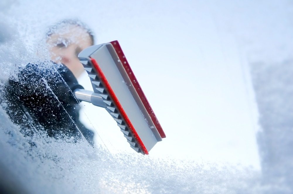Person using a car scraper in winter