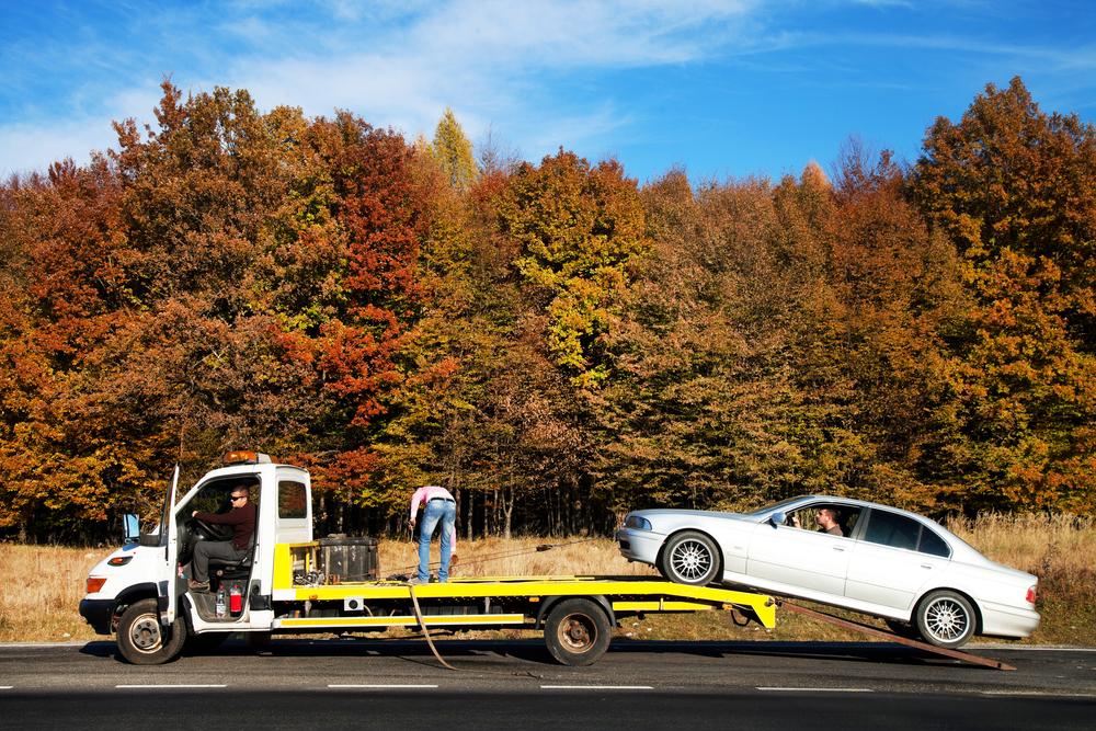 A broken-down car being lifted onto a flatbed tow truck along the motorway