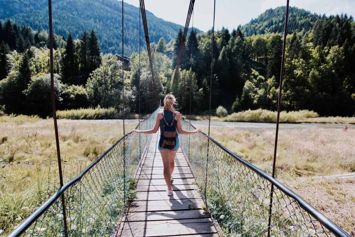 Vrouw alleen op reis steekt een rivier over op een hangbrug