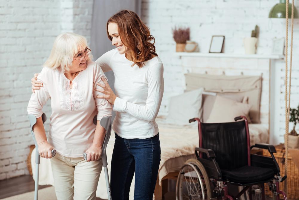 A young woman helps an elderly person with crutches at home