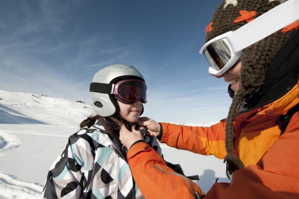 A parent fastens a ski helmet on their son