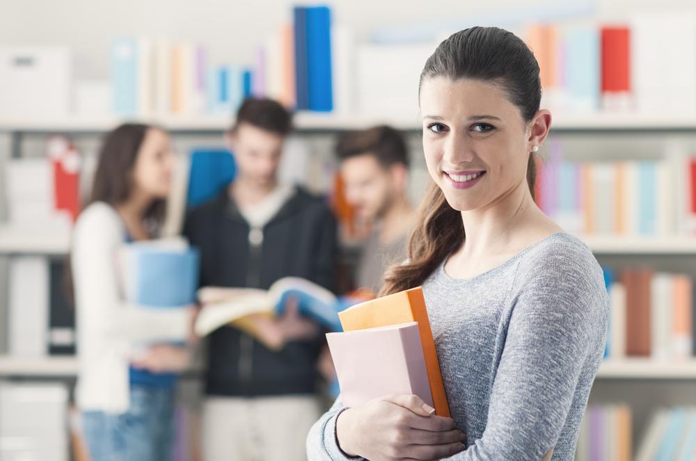 Erasmus student in a library, holding books and smiling