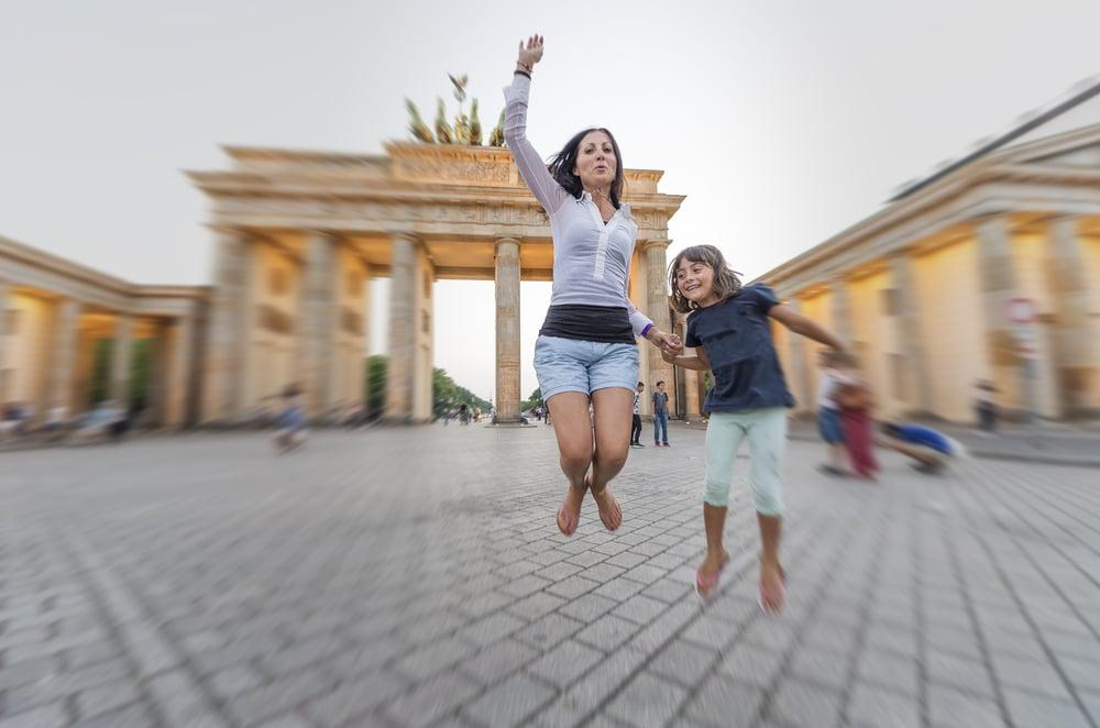 Mother and young girl jumping in front of the Brandenburg Gate in Berlin