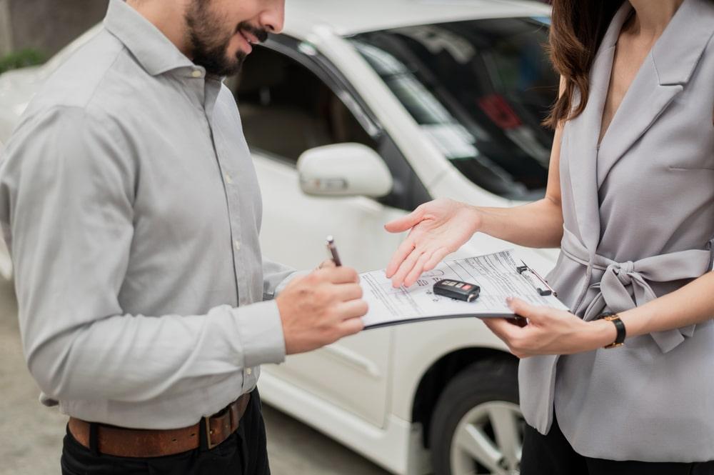 A man signs a car rental agreement. Car in the background
