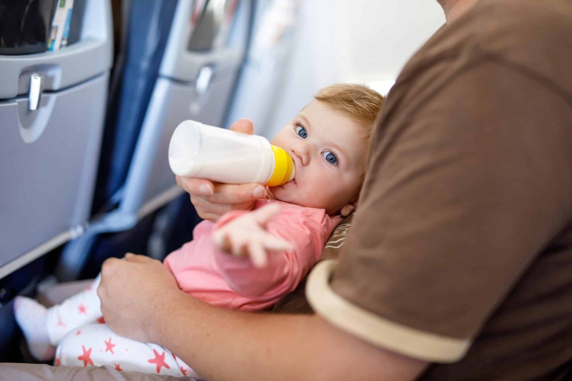 Baby drinking from a bottle on a parent's lap on a plane