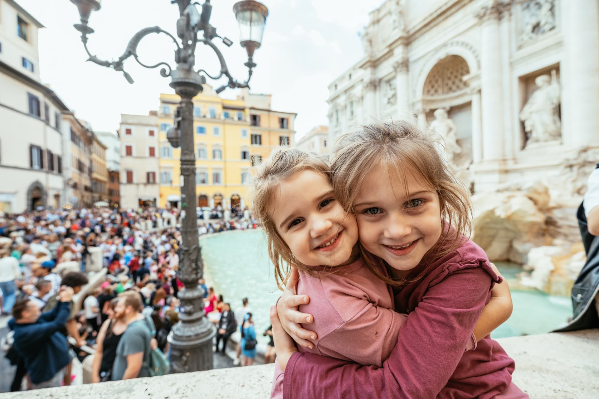 Young children embracing while visiting the Trevi Fountain in Rome