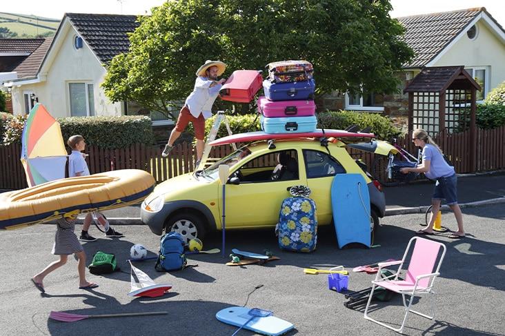 Familie laadt een kleine wagen in voor vertrek op vakantie